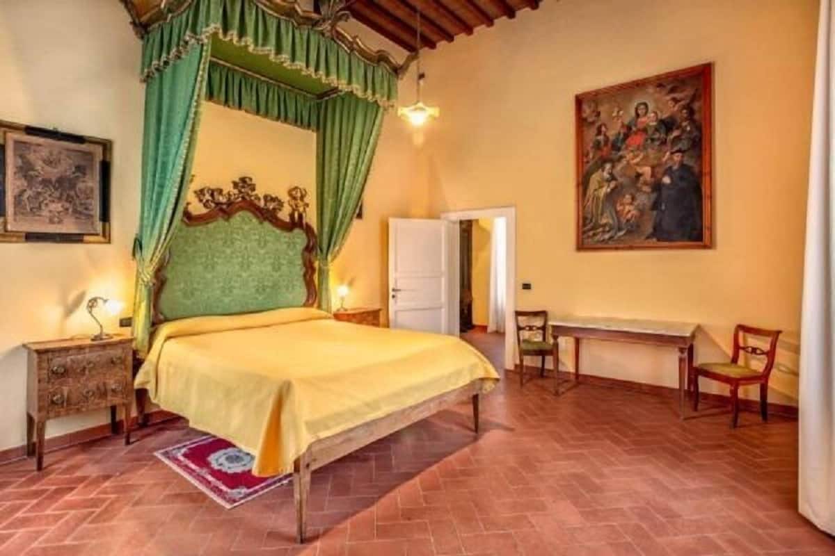 Ein Schlafzimmer mit Bett, Schreibtisch, Stuhl, einem Bild an der Wand und einer Tür.