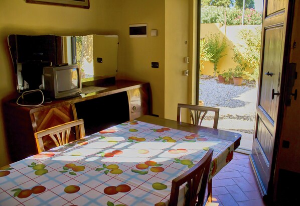 A small kitchen with a table covered in a fruit-patterned tablecloth, a television, and a cabinet. - Agriturismo Villa Graziani (Rosignano Marittimo)