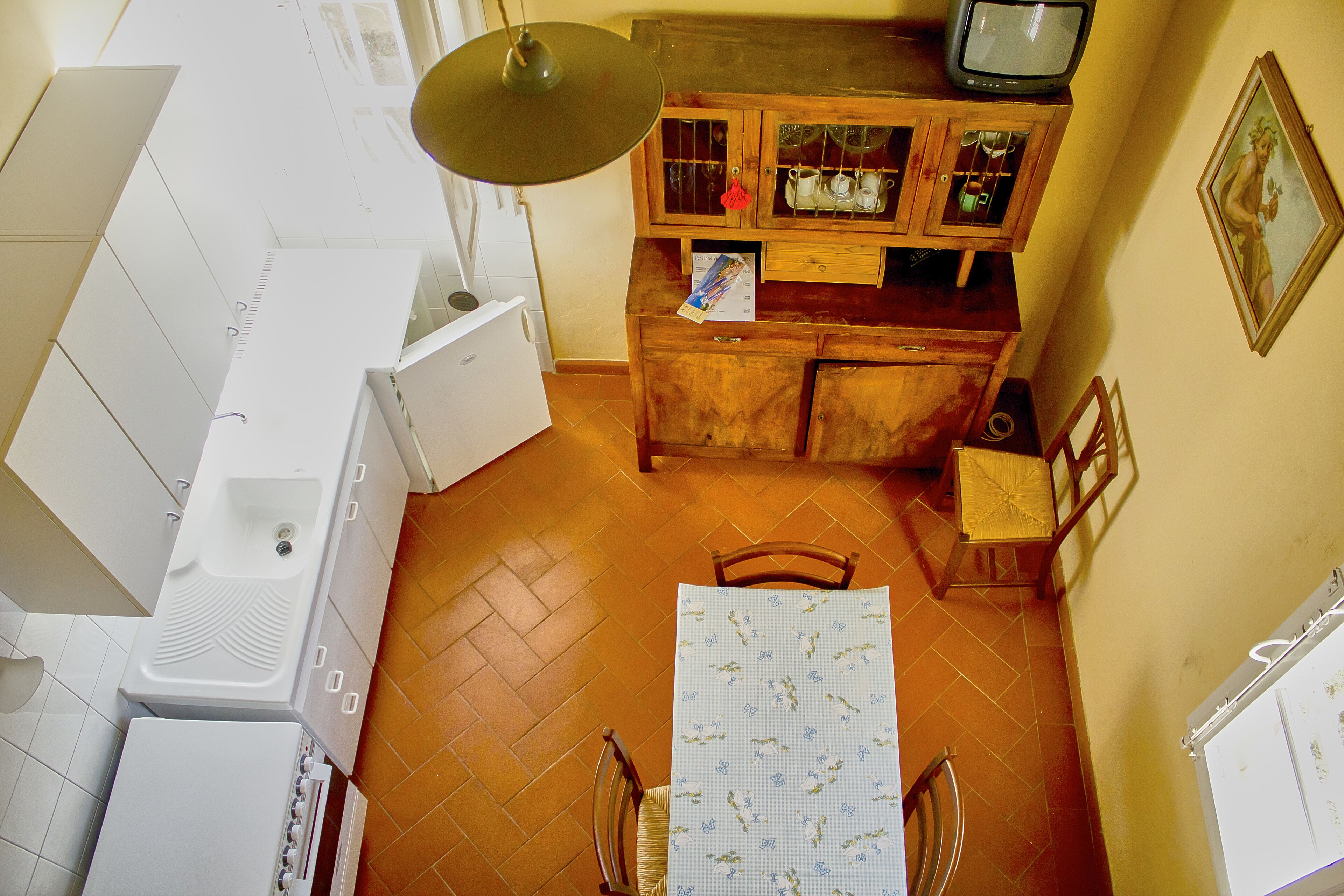 A compact kitchen with white appliances, a wooden cabinet with glass doors, and a dining table with a floral tablecloth.