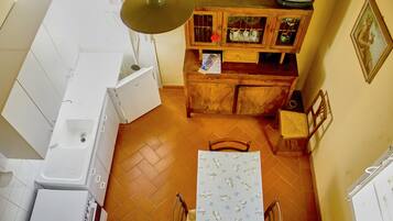 A compact kitchen with white appliances, a wooden cabinet with glass doors, and a dining table with a floral tablecloth.
