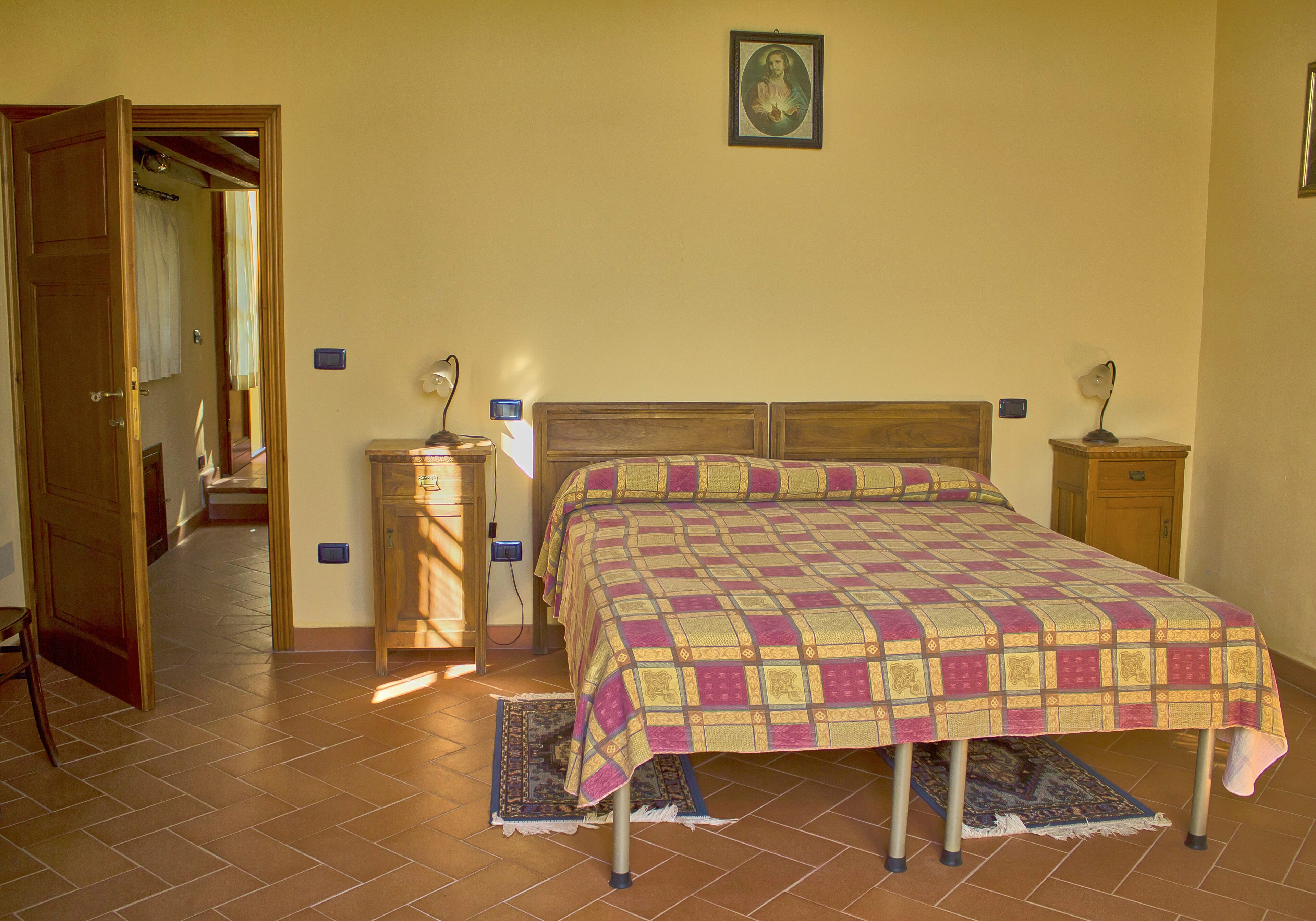 Ein Schlafzimmer mit einem Bett, Holz-Kopfteil, Nachttischen, einem Wandlampen und einer Tür zu einem anderen Raum.