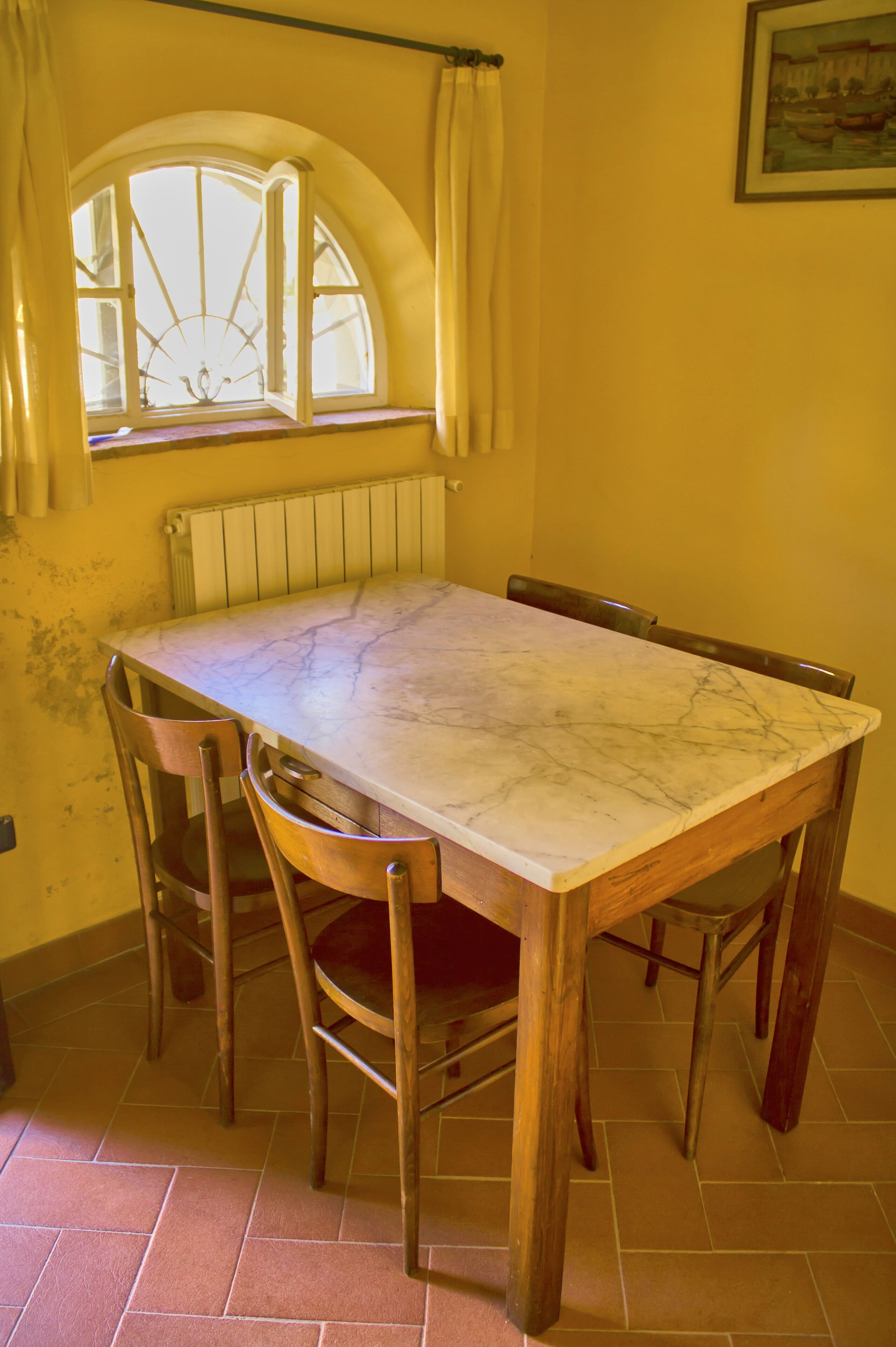 A dining table with four chairs, a window with curtains, and a radiator below.