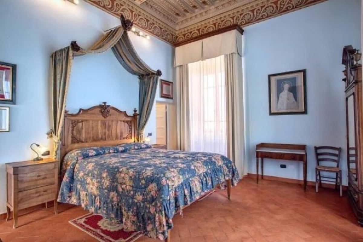 Ein Schlafzimmer mit einem Himmelbett, einem Holfnachtkästchen, einem Schreibtisch und einem Stuhl.
