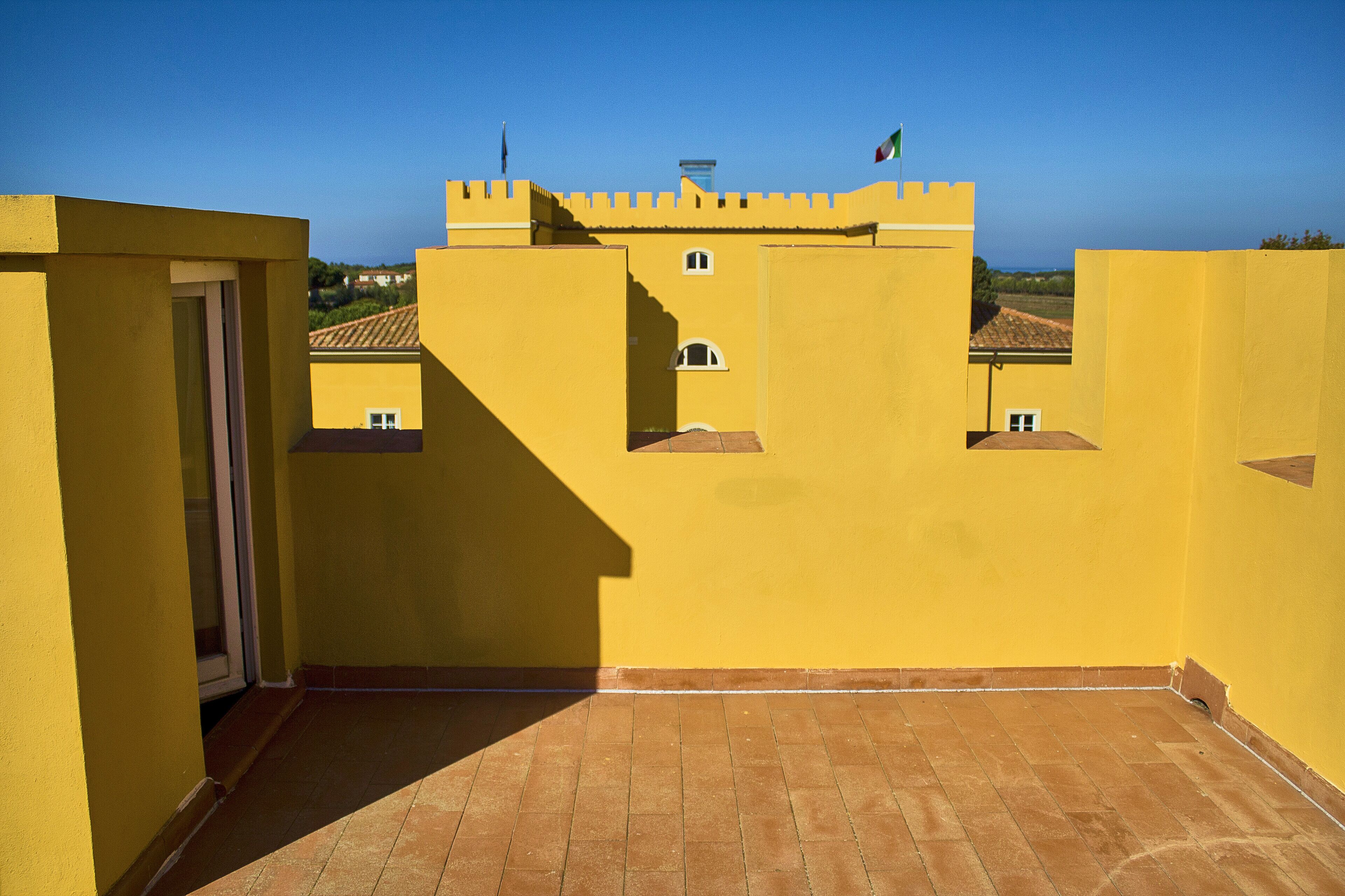 Un bâtiment avec un toit jaune, une petite porte et des fenêtres, un drapeau et un ciel d’un bleu clair.
