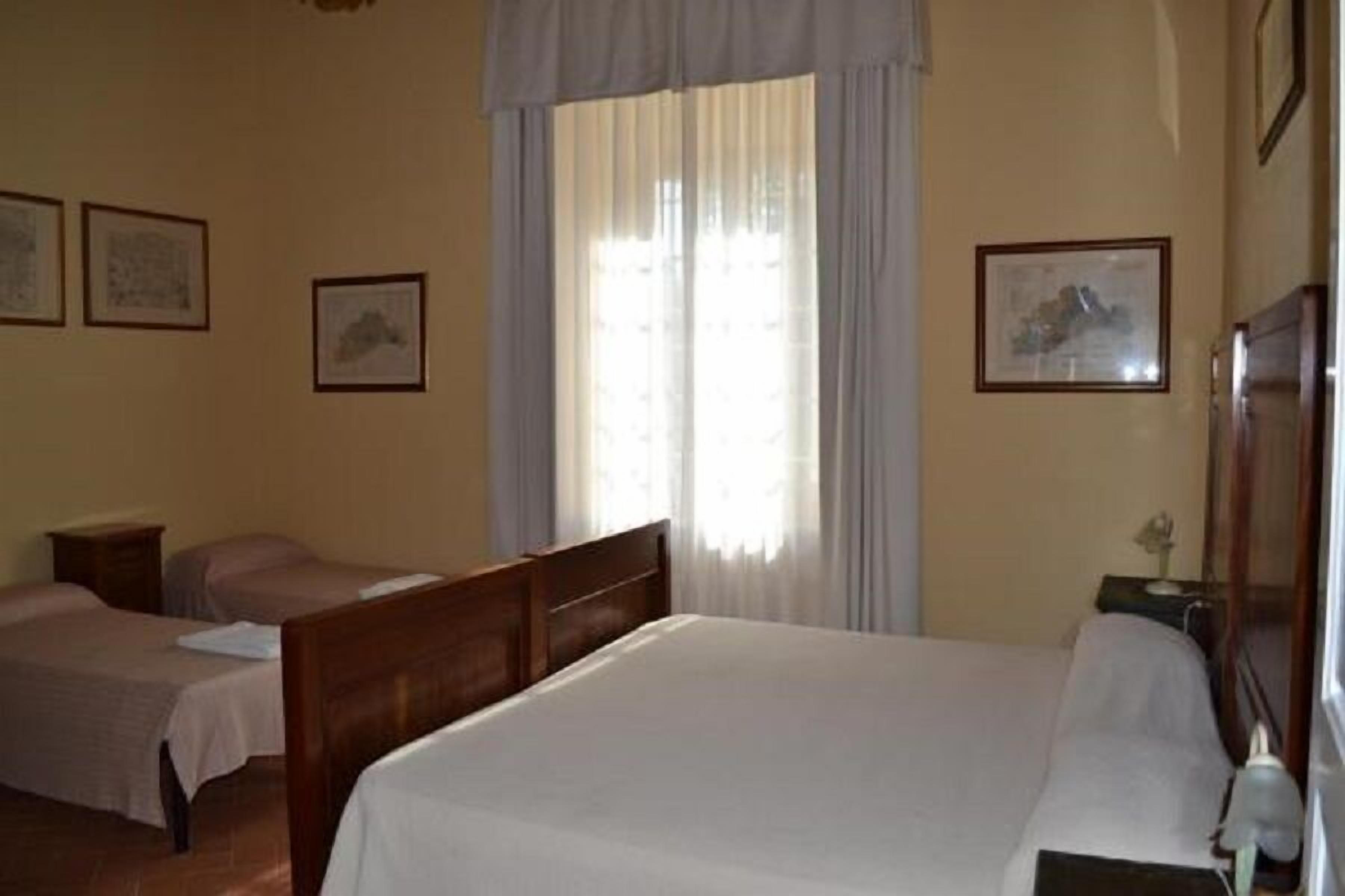 Habitación de hotel con una cama grande, dos camas más pequeñas, una mesita de noche y una ventana con cortinas.