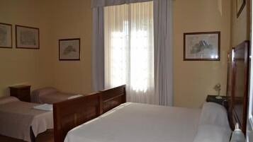 Habitación de hotel con una cama grande, dos camas más pequeñas, una mesita de noche y una ventana con cortinas.