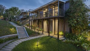 A modern house with a covered outdoor area, a staircase leading to a deck, and a well-maintained garden. - Ragamaya Resort & Spa Munnar (Udumbanchola)
