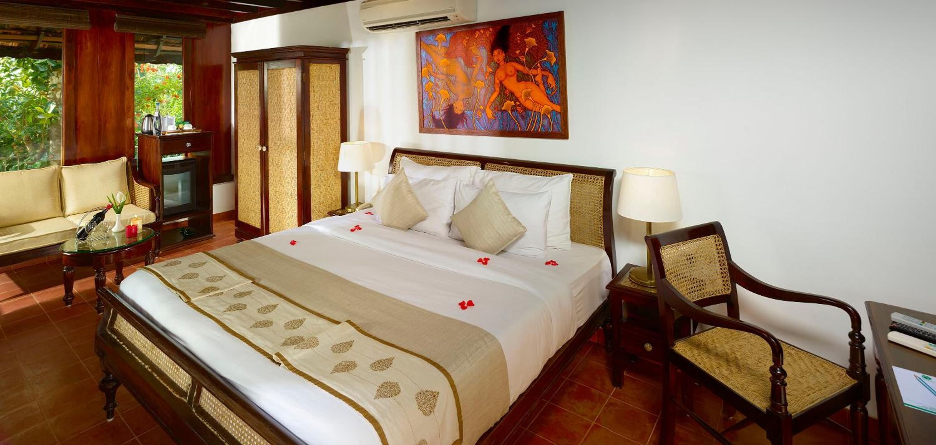 A hotel room with a bed, two bedside tables, a chair, a sofa, and a painting on the wall.