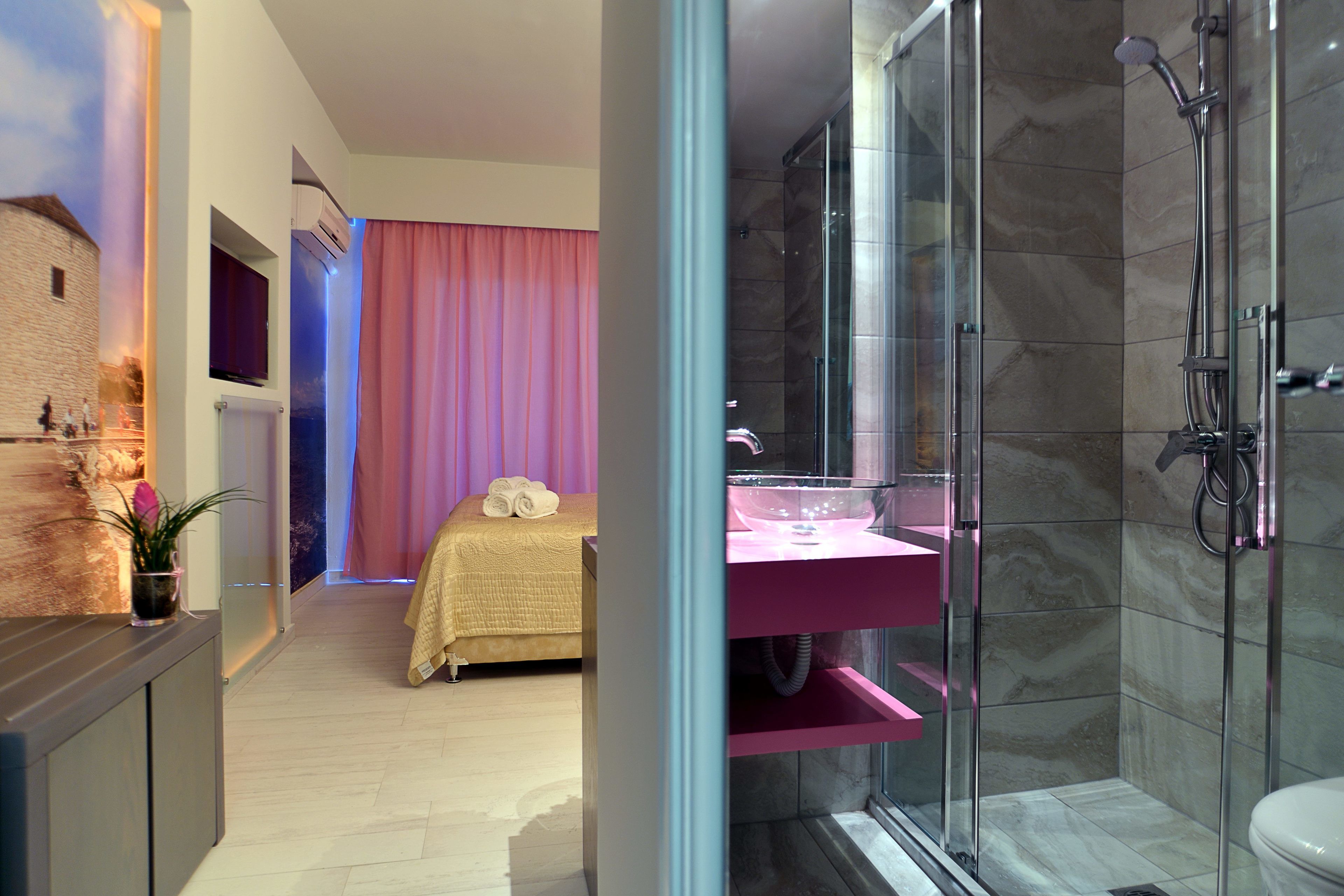 Ein modernes Hotelzimmer mit einem Bett, einem rosa Schminktisch, einer Dusche und einem großen Fenster.
