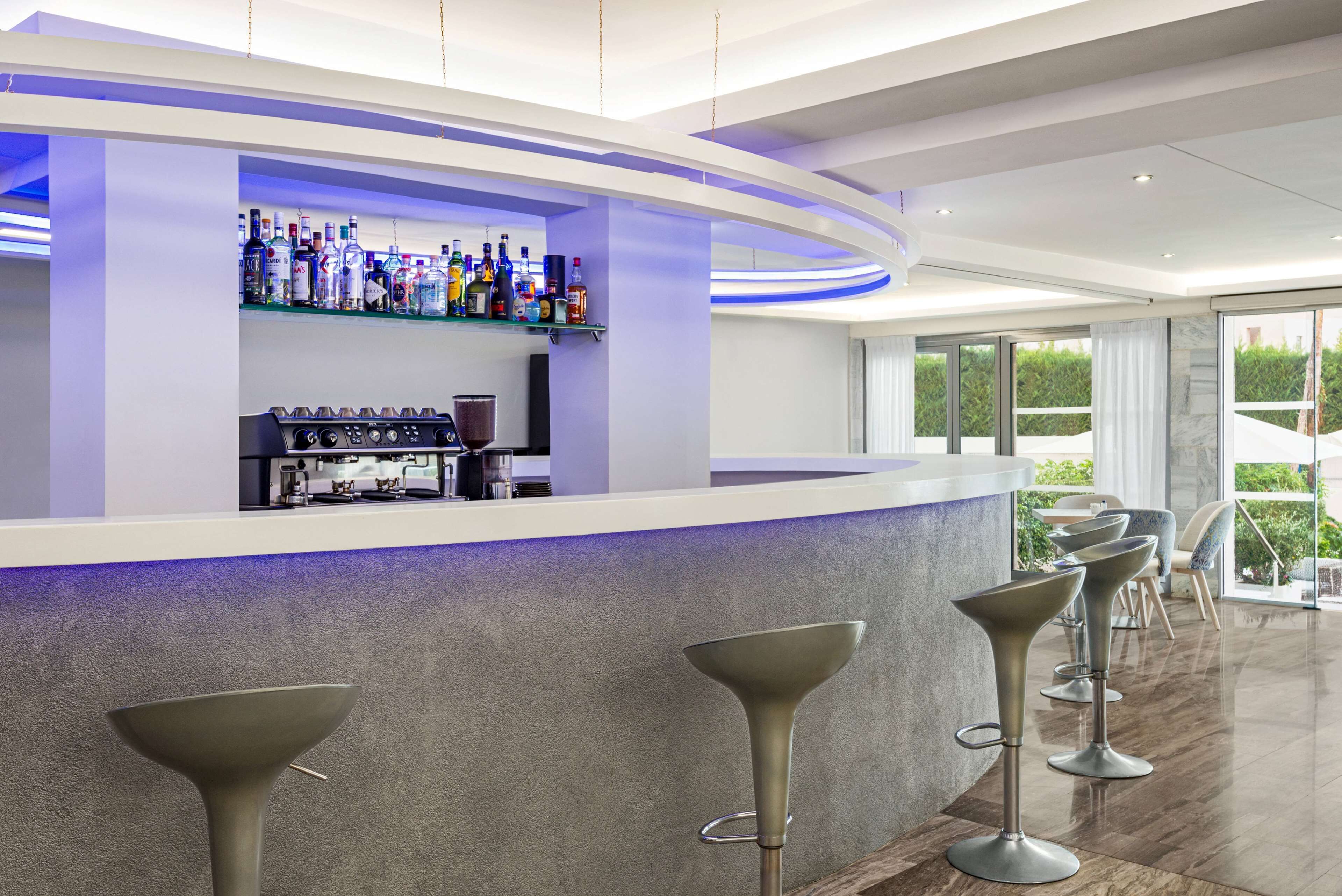 Un espace bar moderne doté d’un comptoir incurvé, de tabourets de bar et d’une variété de bouteilles d’alcool.