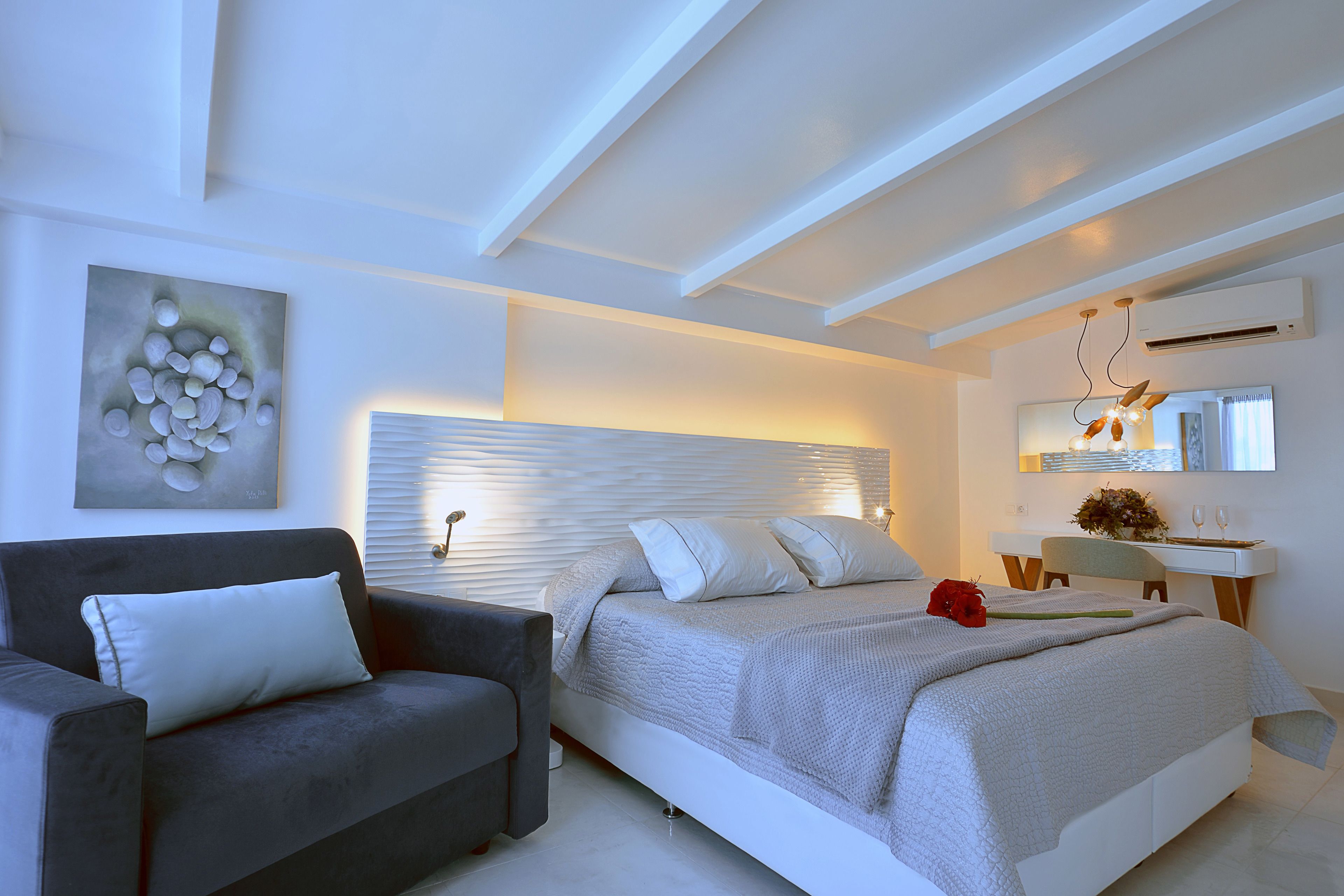 A modern bedroom with a bed, a sofa, a bedside table, and a wall-mounted air conditioning unit.