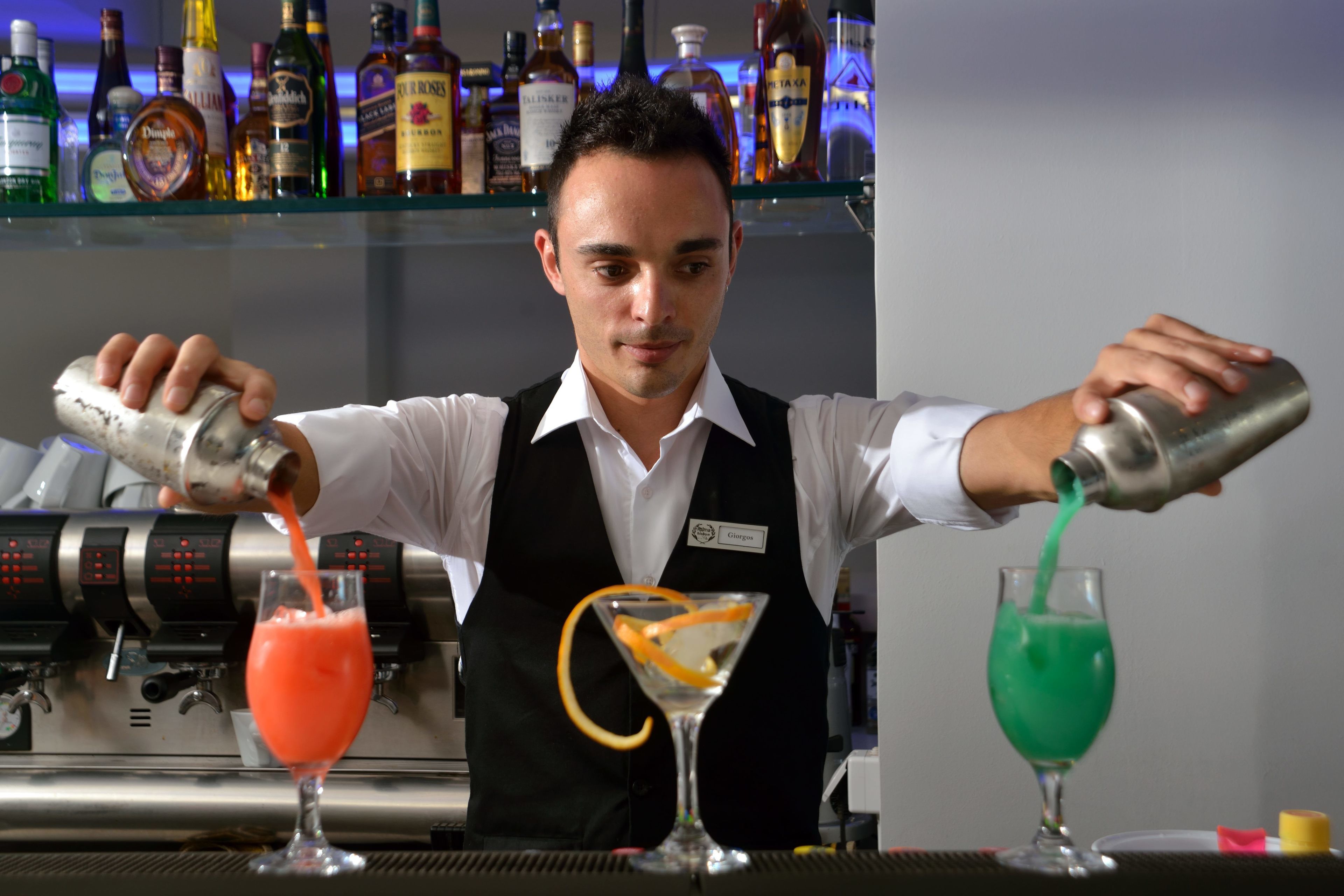 A bartender pouring drinks into martini glasses.