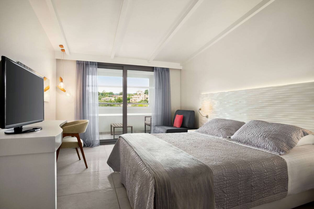 Een moderne hotelkamer met een groot bed, een flatscreen televisie, een bureau en een balkon met uitzicht.