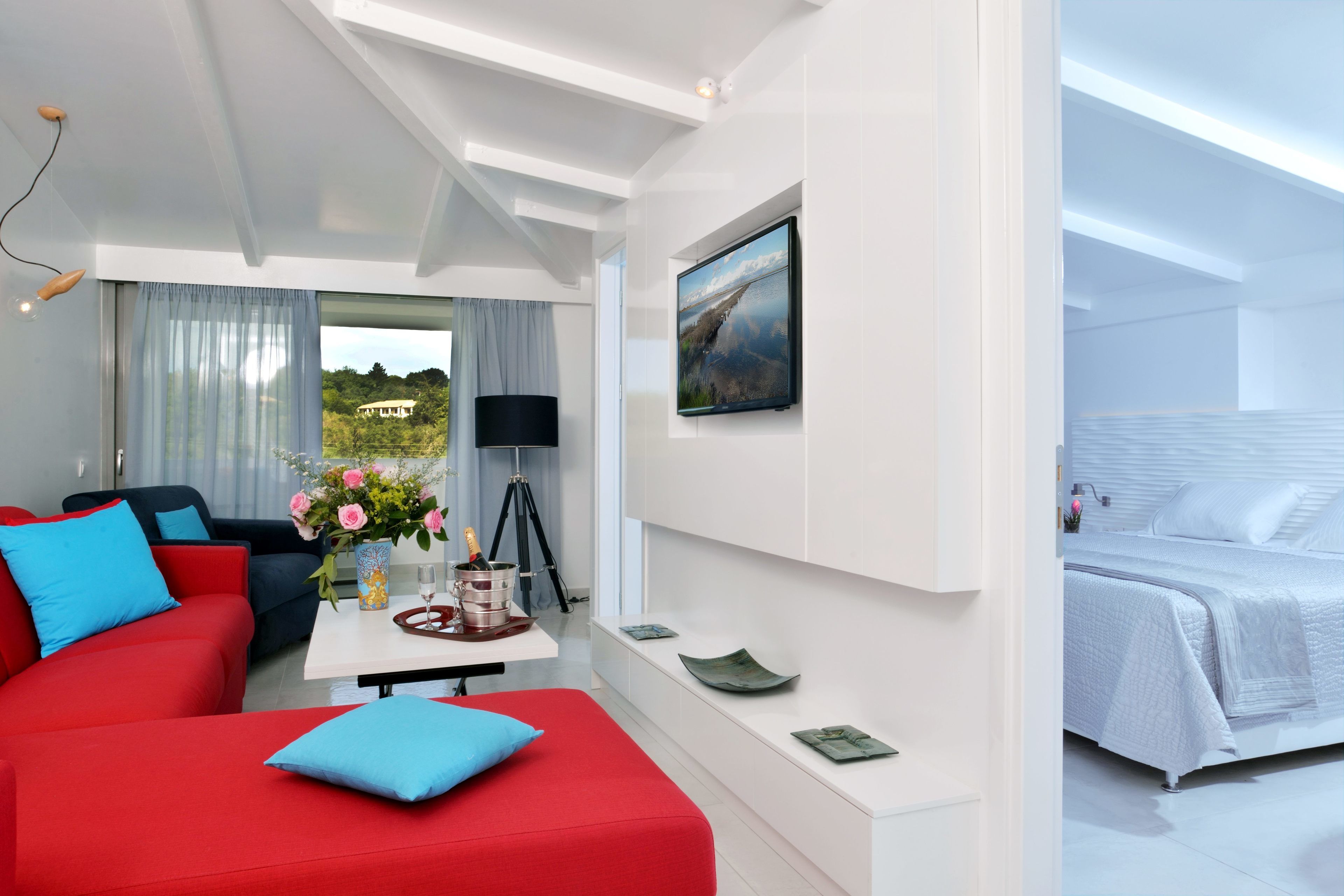 Una camera d'albergo moderna con un divano rosso, un letto bianco e un'ampia finestra che si affaccia sul verde.