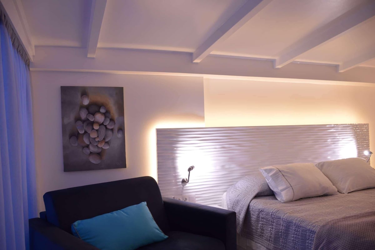 Een moderne kamer met een bed, een slaapbank, een kunstwerk aan de muur en een plafond met zichtbare balken.