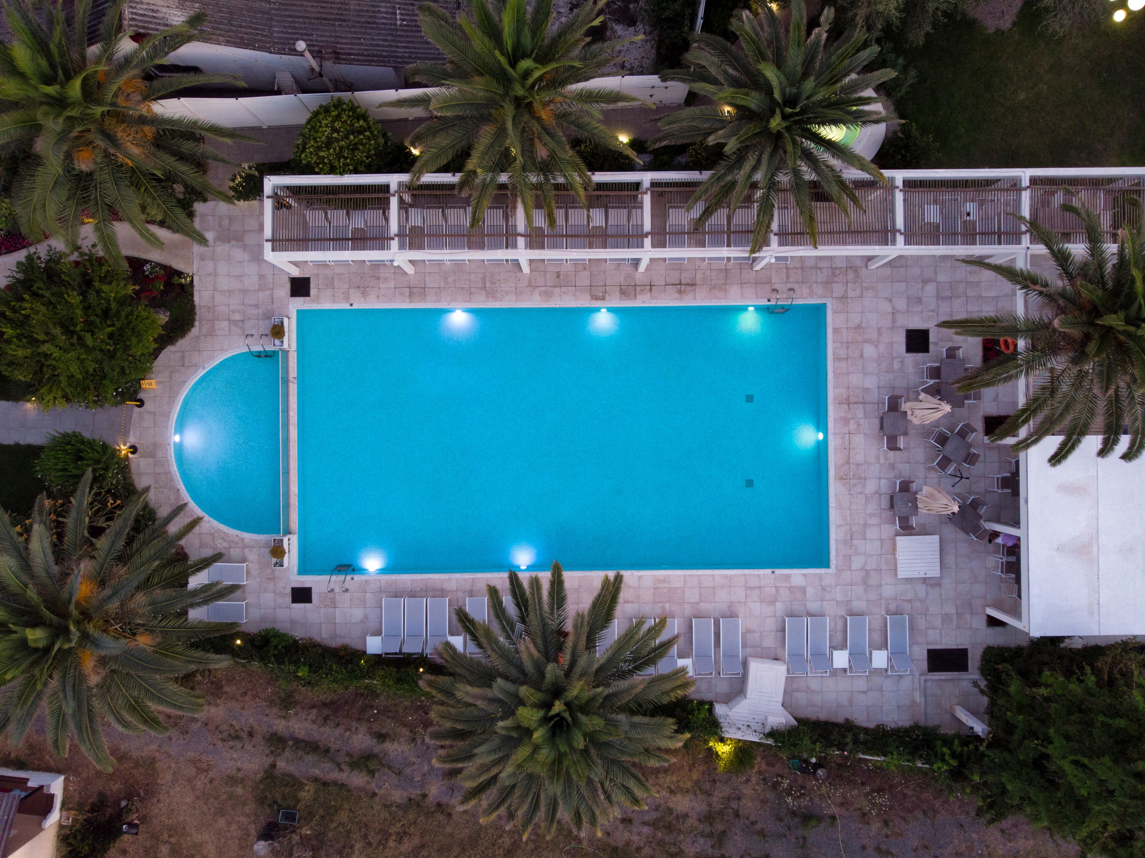 A rectangular swimming pool with a tiled deck surrounding it, equipped with multiple lounge chairs and umbrellas.