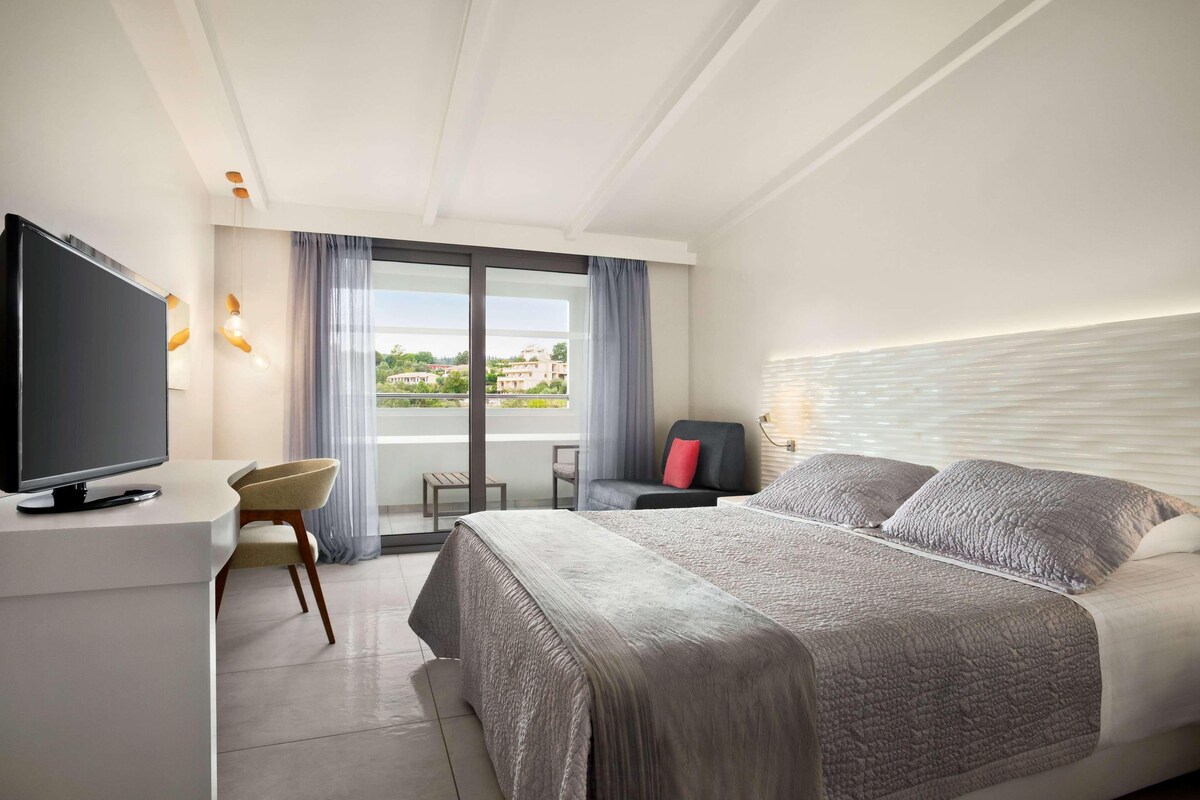 Quarto de hotel moderno com uma cama grande, televisão de tela plana, escrivaninha e vista para o exterior.