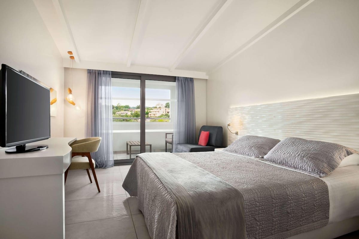 Een moderne hotelkamer met een groot bed, een flatscreen televisie, een bureau en uitzicht op de omgeving.