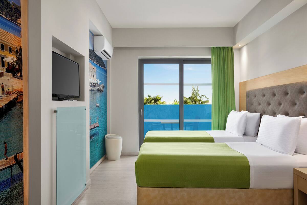 Een hotelkamer met een bed, een televisie, een schilderij en een balkon met uitzicht.