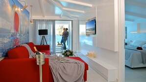 Une chambre d’hôtel moderne avec un canapé rouge, un lit, un téléviseur fixé au mur et un balcon offrant une vue sur la mer.