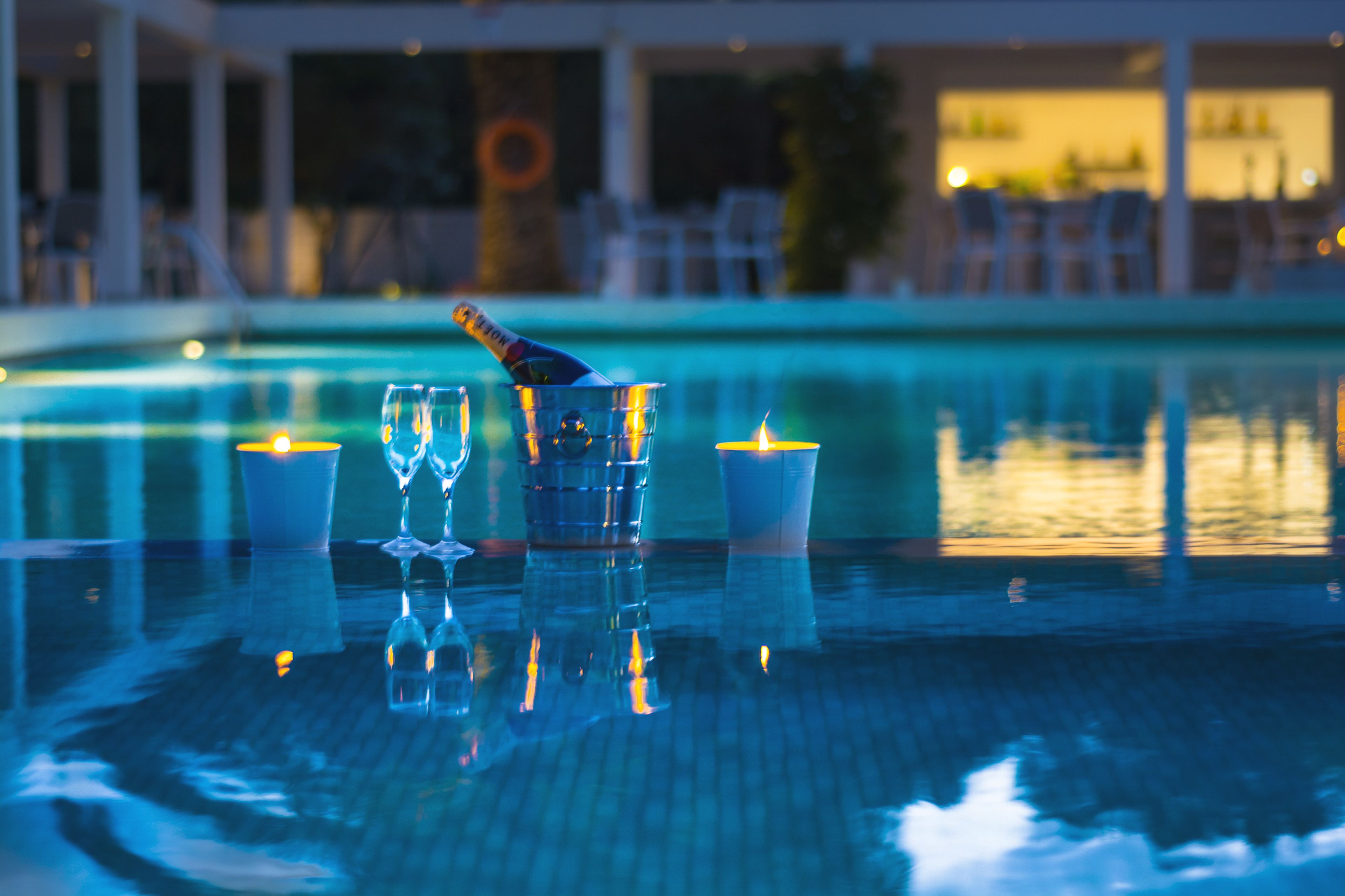 Una mesa junto a la piscina con una botella de champán, dos copas y dos velas.