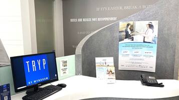 A reception desk with a computer monitor displaying 'TRYP BY WYNDHAM', a phone, and informational posters.
