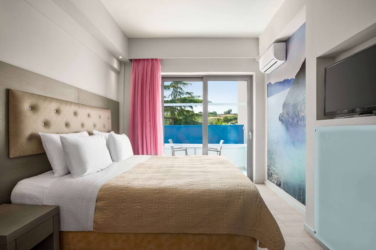 Een hotelkamer met een bed, een televisie, een balkon met uitzicht en een airconditioning.