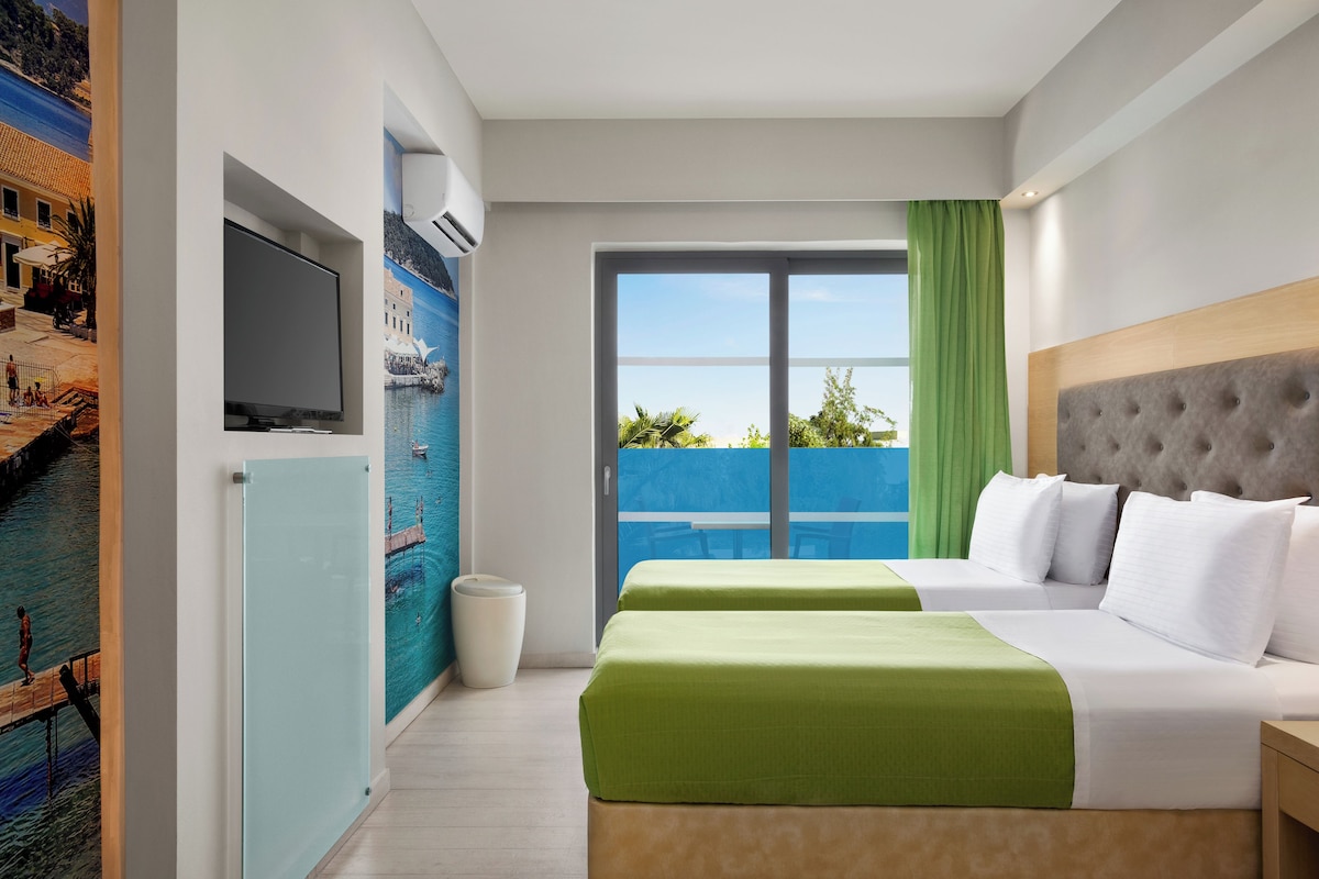 Een hotelkamer met een bed, een televisie, een schilderij en een balkon met uitzicht.