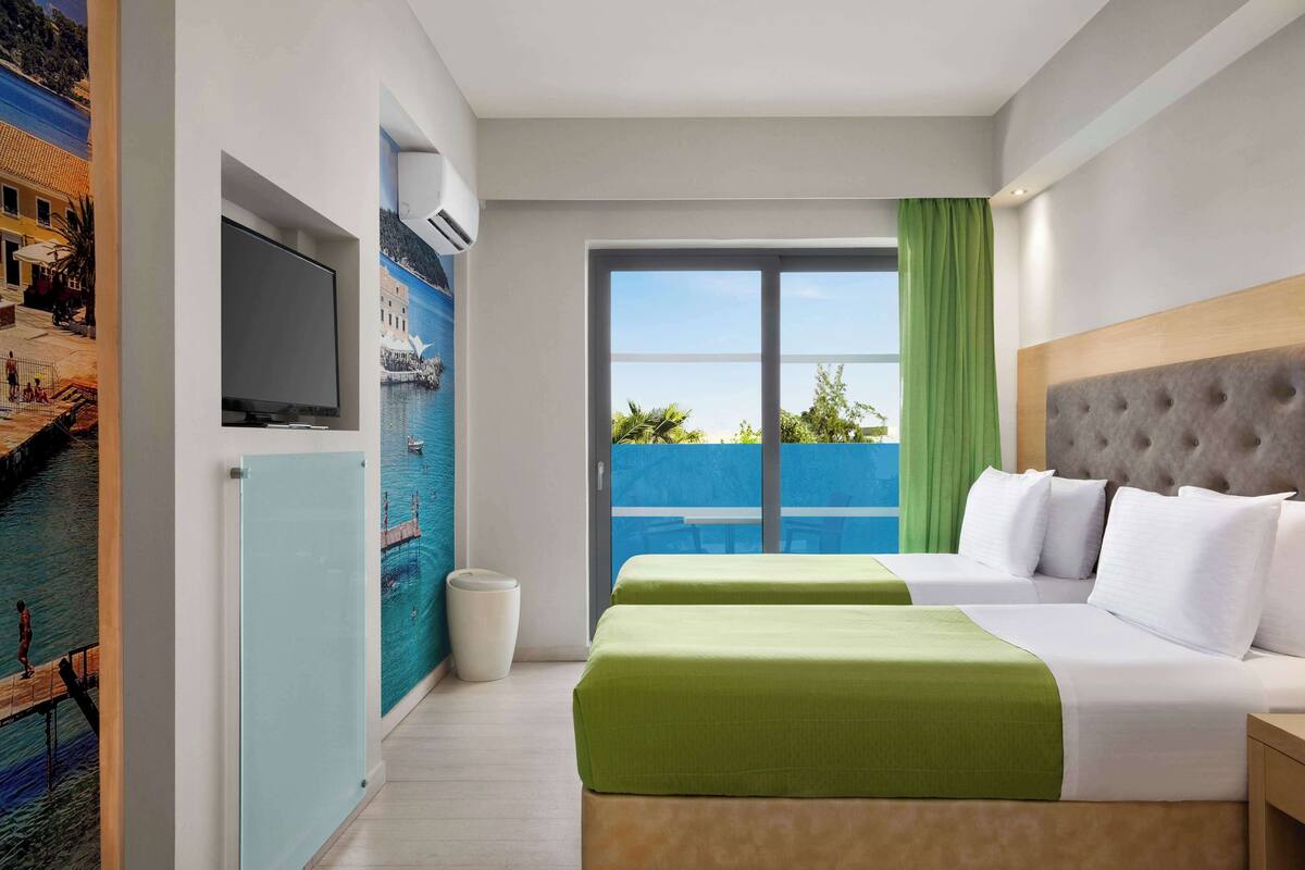 Hotelkamer met een bed, televisie, muurschildering, balkon met uitzicht en een raam met gordijnen.