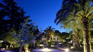 Un jardin aménagé avec une fontaine circulaire, des palmiers et un bâtiment en arrière-plan.