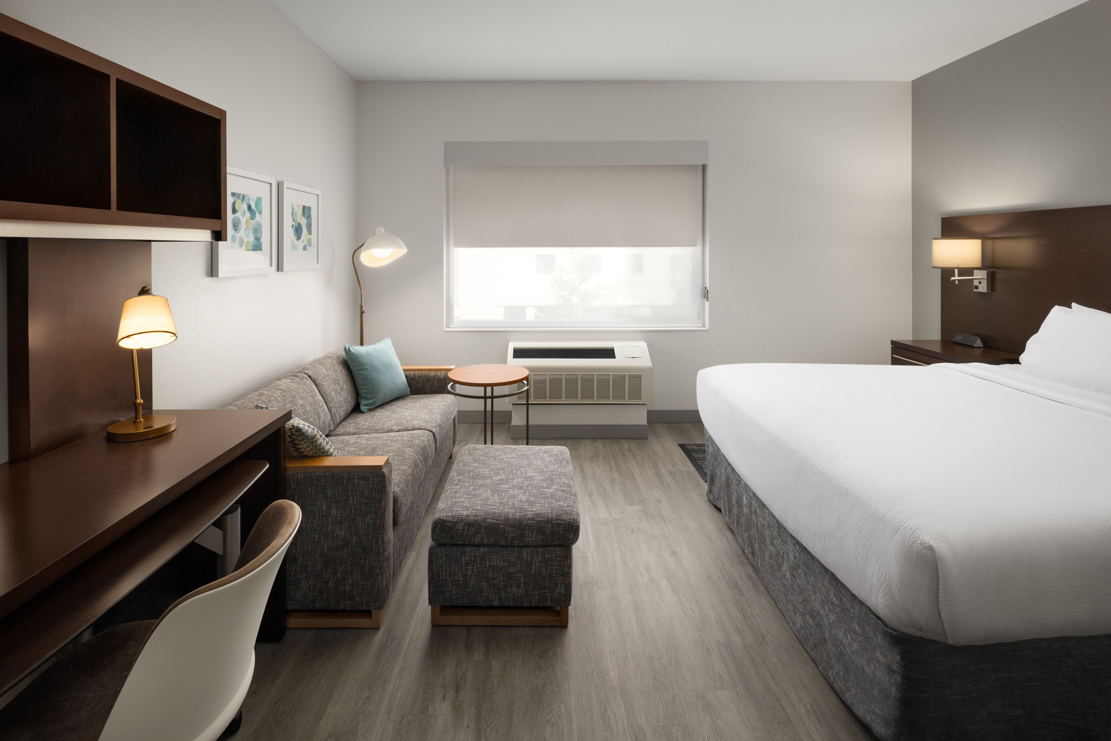 Une chambre d’hôtel avec un lit, un canapé, une petite table, un bureau, une chaise et une fenêtre avec des stores.
