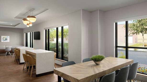 A modern conference room with a wooden table, grey chairs, a potted plant, and large windows offering a view of the street. - Towneplace Suites Anchorage Midtown (Anchorage)