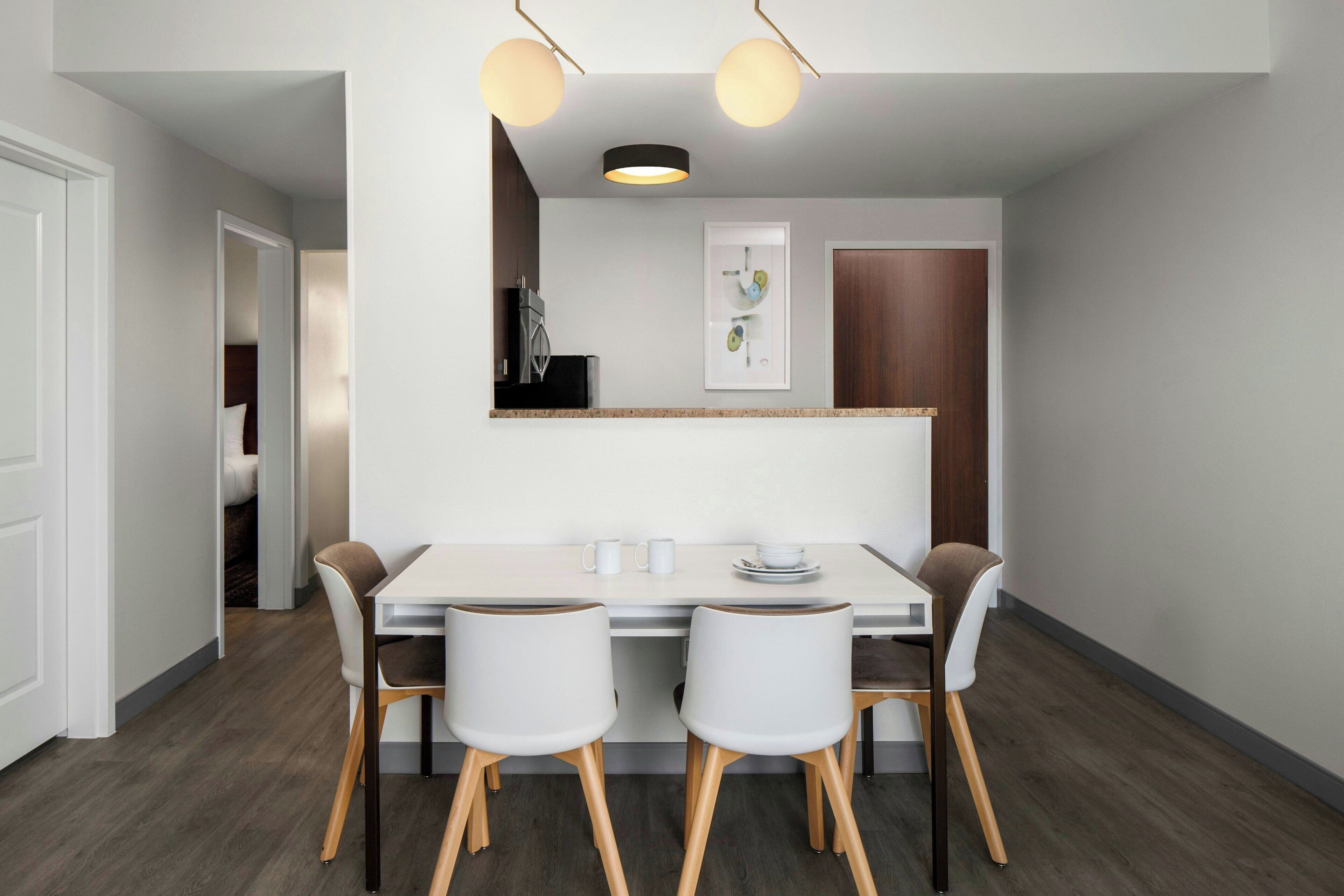 A modern kitchen with a white countertop, two white chairs, and a wooden dining table.