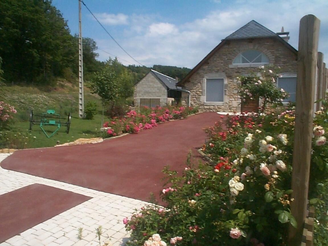 Un bâtiment en pierre avec une allée rouge et un jardin agrémenté de fleurs roses et blanches.