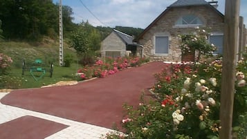 Un bâtiment en pierre avec une allée rouge et un jardin agrémenté de fleurs roses et blanches.