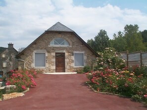 A stone house with a triangular roof, a central door, and a red driveway. - Hôtel & Spa Rodier (Campagnac)