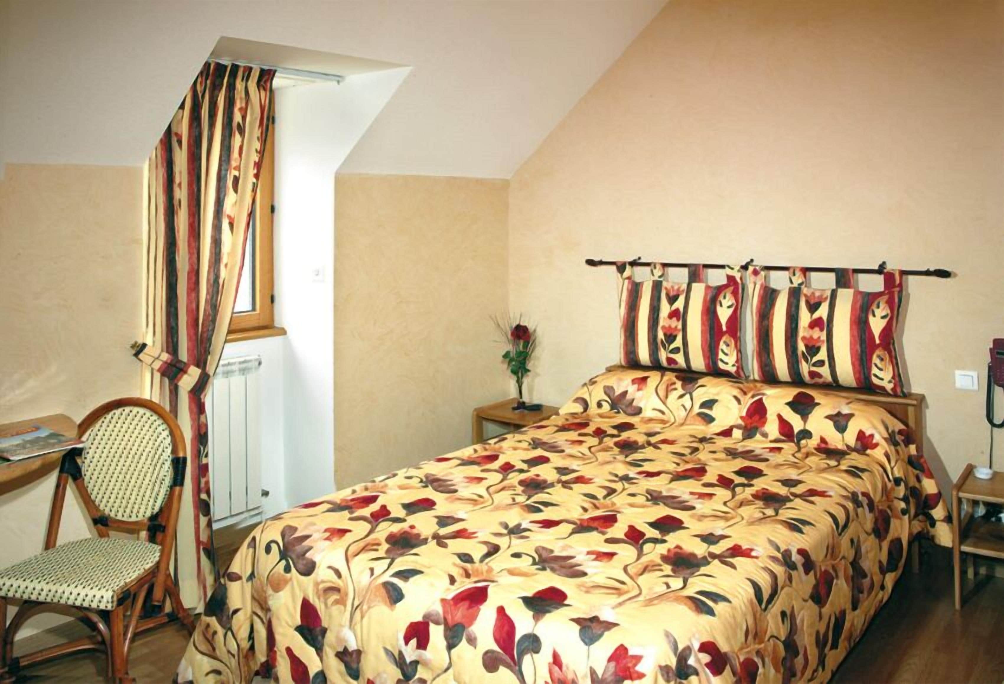 Une chambre à coucher avec un lit, une chaise, une table de chevet, une fenêtre et un rideau.