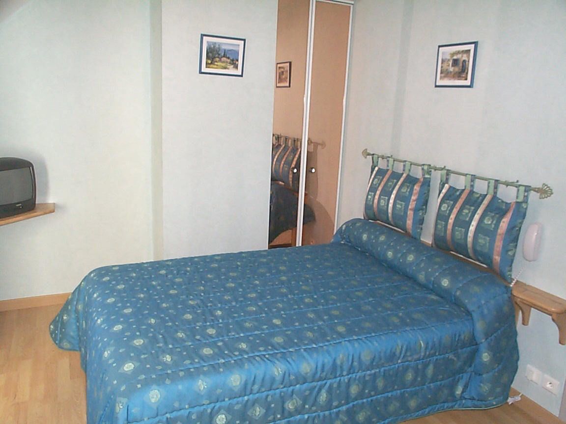 A bedroom with a bed, a wardrobe, and a small shelf with a television.