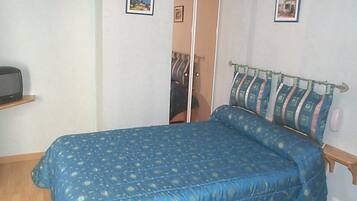 A bedroom with a bed, a wardrobe, and a small shelf with a television.