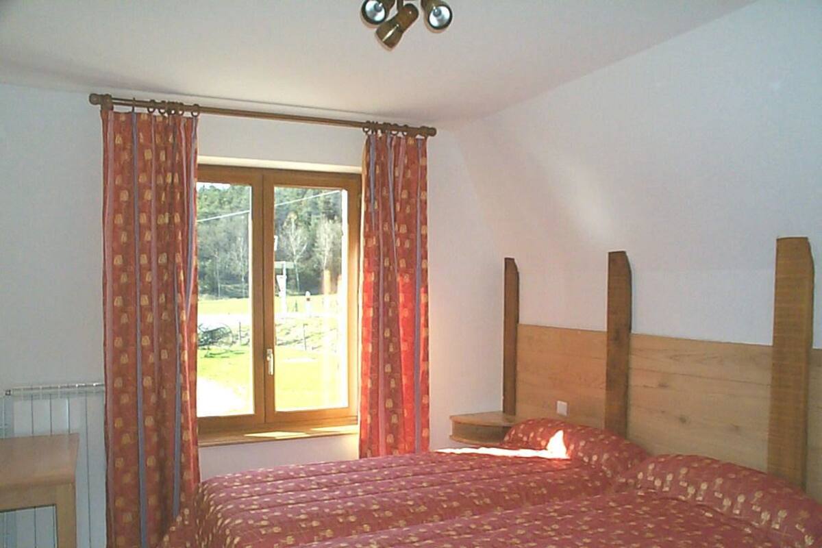 A bedroom with two beds, a wooden headboard, a window with curtains, and a radiator.