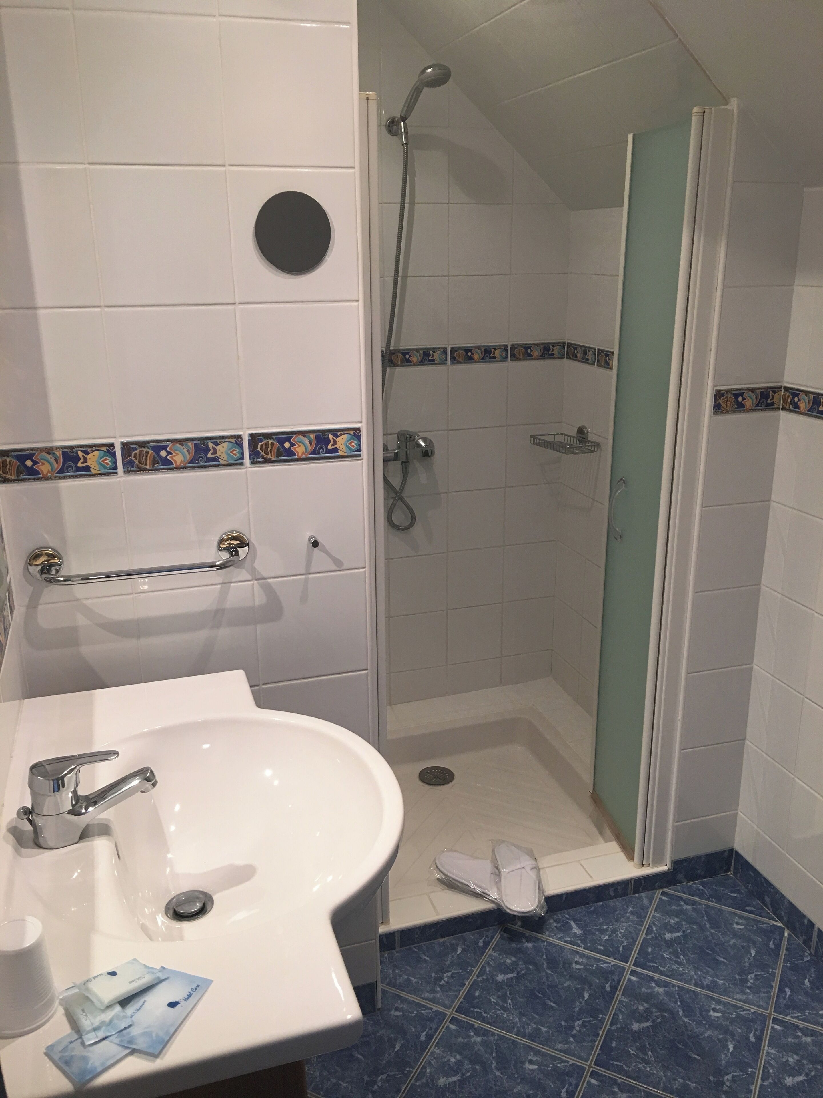 Un baño con lavamanos blanco, ducha con puerta de vidrio y paredes con azulejos azules.