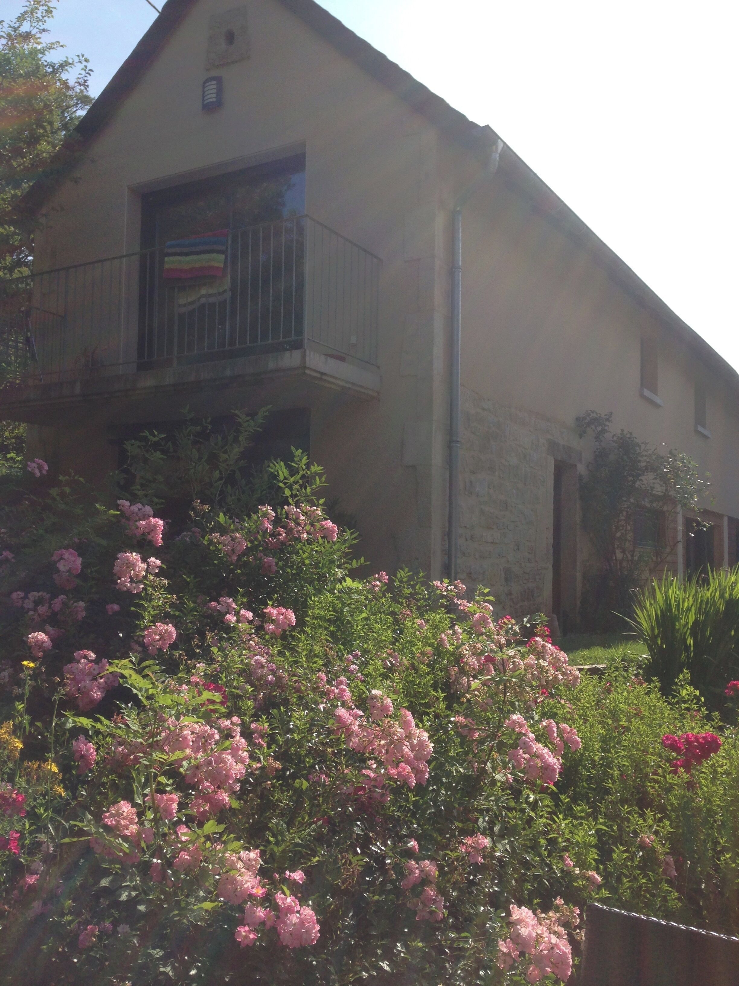 A two-story building with a balcony and a garden with pink flowers.