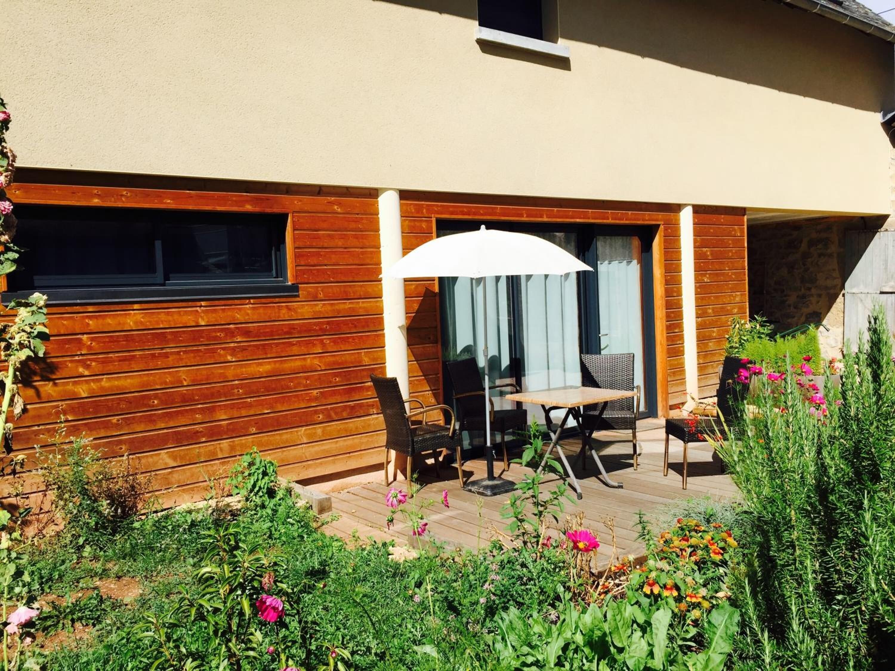 Una casa de madera con un patio que tiene una mesa y sillas bajo un paraguas blanco.