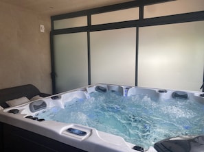 Un jacuzzi con panel de control, rodeado por un sofá de color oscuro y una pared con un panel de vidrio esmerilado.