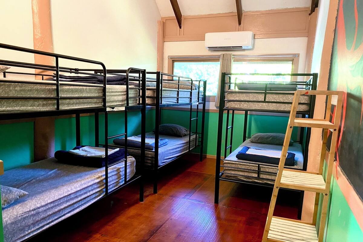 A dormitory room with bunk beds, a wooden ladder, and an air conditioning unit.