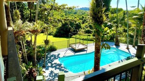 Zona de piscina con vista a un jardín exuberante y colinas distantes.