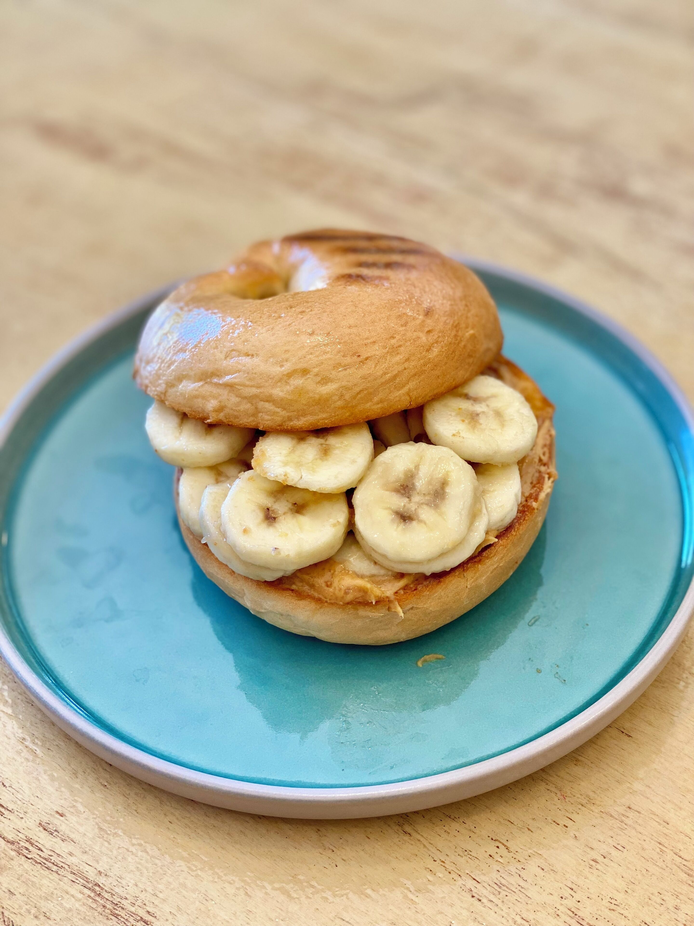 A bagel with banana slices on a blue plate.