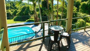 Terraza de madera con piscina, sillas y vistas a un paisaje tropical.