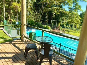 A wooden deck with a glass table and chairs overlooking a swimming pool. - Jackaroo Treehouse Mission Beach - Hostel (Bingil Bay)