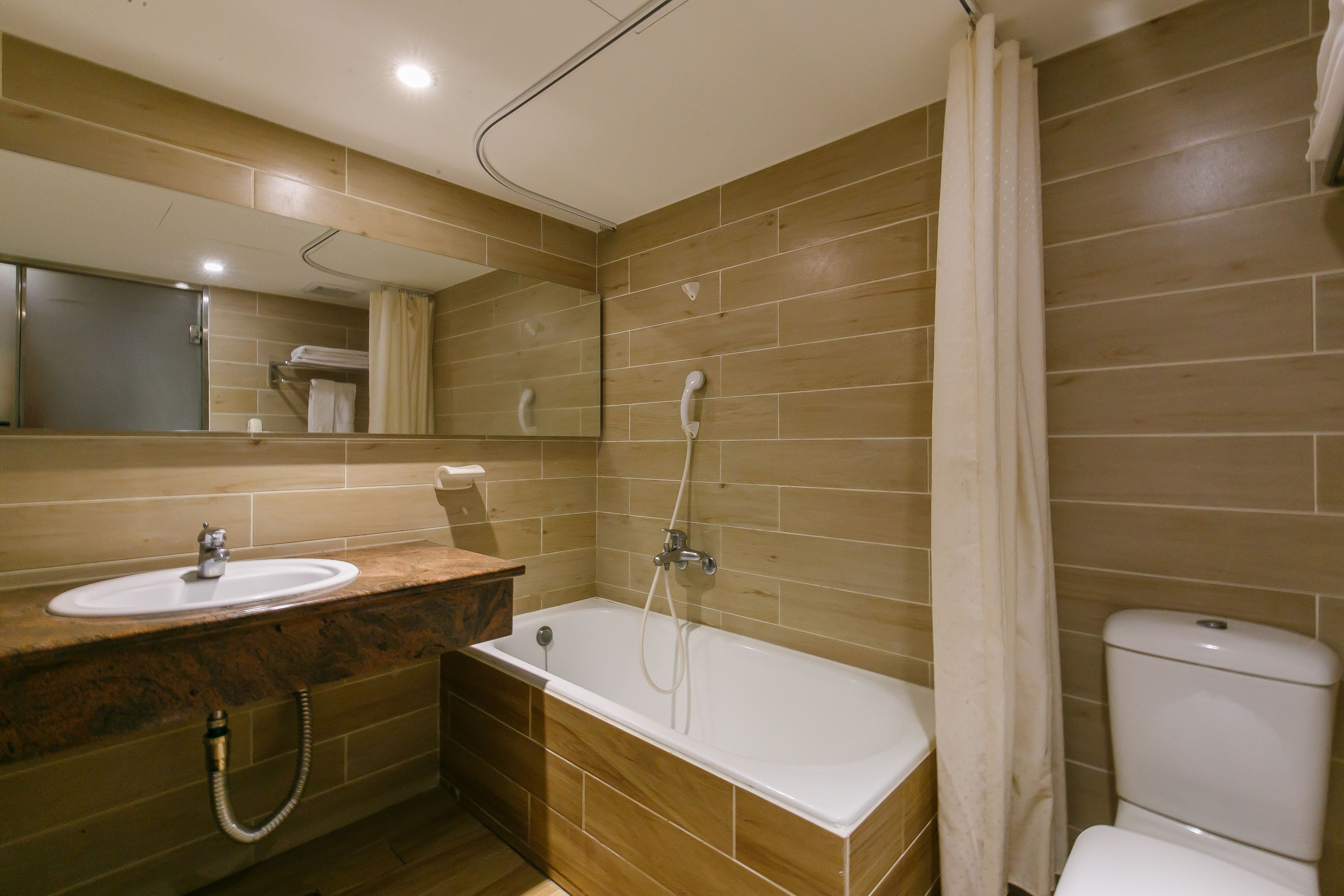 Ein modernes Badezimmer mit einem Holzkosmetikschrank, einer Badewanne, einer Toilette und einem Spiegel.